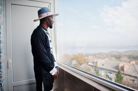 Rich african man looking at panoramic window at his penthouse. Portrait of successful black man in...