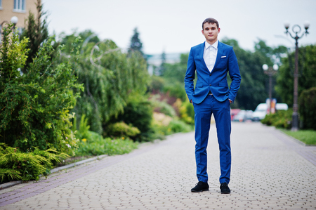 Portrait of a handsome young man in formal fancy suit posing on the pavement in the park on a prom day.の写真素材