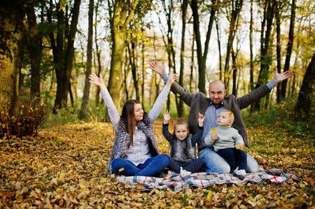Happy caucasian family of mom dad and little girl with boy sitting on plaid at majestic autumn fall forest.の写真素材