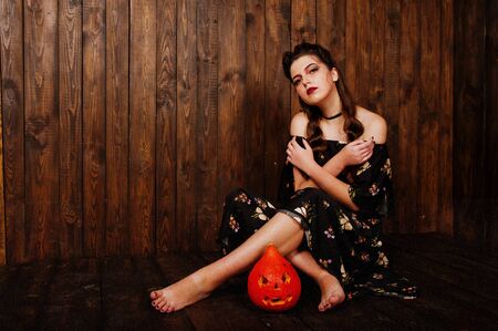 Black girl in dress with bright make-up and pumpkin against wooden background. Halloween theme.の写真素材