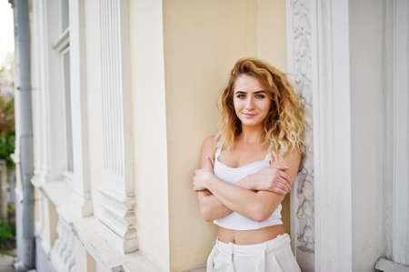 Stylish curly blonde model girl wear on white posing against old vintage house.の写真素材