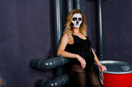 Halloween skull make up girl wear in black against sitting on red barrel at studio.の写真素材