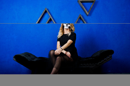 Halloween skull make up girl wear in black against blue wall at studio.
