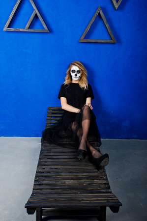 Halloween skull make up girl wear in black against blue wall at studio.の写真素材