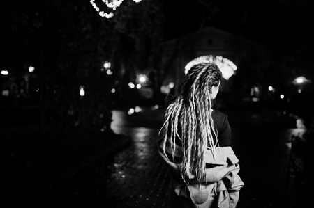 Girl with dreadlocks walking at night street of city against garland lights.の写真素材