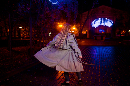 Girl with dreadlocks walking at night street of city against garland lights.の写真素材