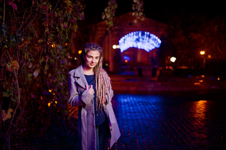 Girl with dreadlocks walking at night street of city against garland lights.の写真素材