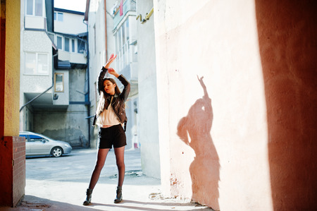 Stylish brunette girl wear on leather jacket and shorts against orange wall at shadows.の写真素材
