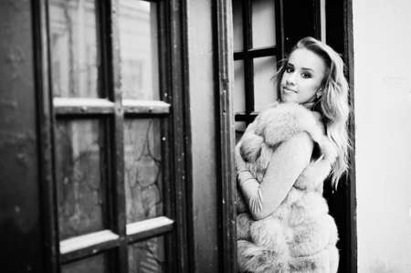 Blonde girl at fur coat posed against old wooden door.の写真素材