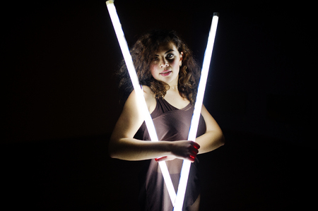 Curly brunette plus size model with two long led lamp at black room.の写真素材