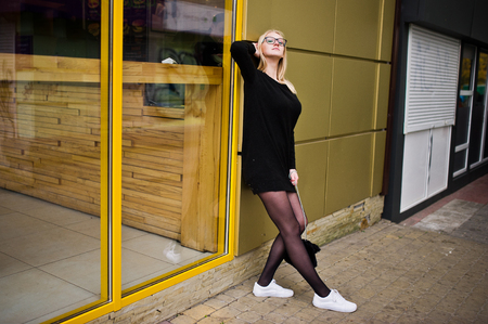 Blonde girl at glasses and black tunic posed against yellow windows.の写真素材