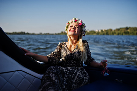 Blonde girl in wreath sitting on yacht at hen party with champagne.の写真素材