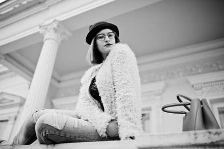 Red haired girl in glasses and hat with red handbag posed near vintage house.の写真素材