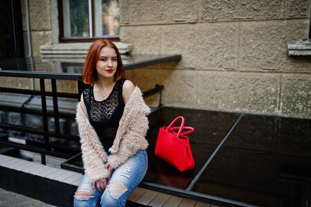 Red haired girl with red handbag posed at street of city.の写真素材