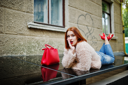 Red haired girl with red handbag posed at street of city.の写真素材