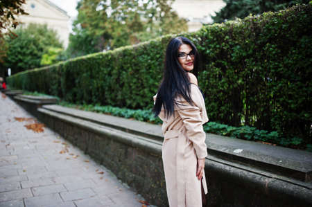 Black hair sexy woman in glasses and coat posed on street.