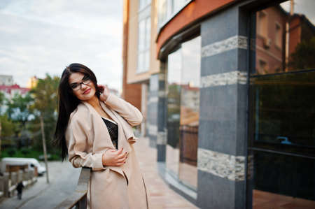 Black hair sexy woman in glasses and coat posed against building with modern windows.の写真素材