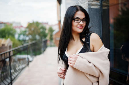 Black hair sexy woman in glasses and coat posed against building with modern windows.の写真素材