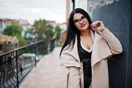 Black hair sexy woman in glasses and coat posed against building with modern windows.の写真素材