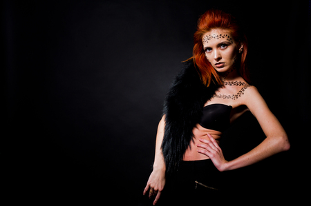 Fashion model red haired girl with originally make up like leopard predator isolated on black. Studio portrait.の写真素材