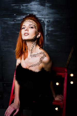 Fashion model red haired girl with originally make up like leopard predator against steel wall. Studio portrait on ladder.の写真素材