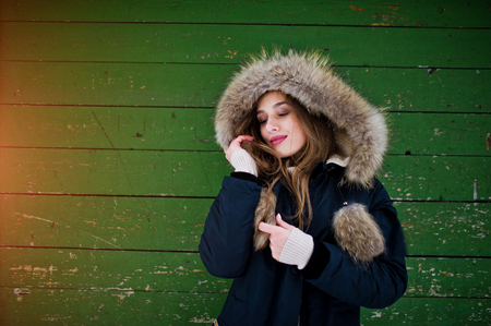Beautiful brunette girl in winter warm clothing. Model on winter jacket against green wooden background.の写真素材