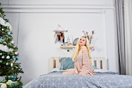 Elegante blonde girl wear on warm tunic sitting on bed.の写真素材