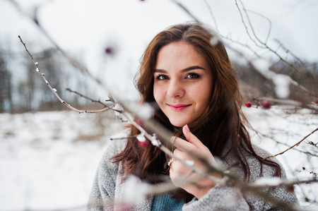 Close up portrait of gentle girl in gray coat near the branches of a snow-covered tree.の写真素材