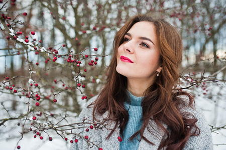 Close up portrait of gentle girl in gray coat near the branches of a snow-covered tree.の写真素材
