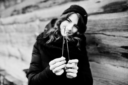 Portrait of brunette curly girl in black jacket, hat and scarf with bengal lights in hand.の写真素材