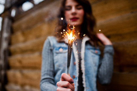 Portrait of brunette girl in jeans jacket with bengal lights in hands.