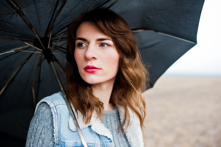 Portrait of brunette curly girl in jeans jacket with black umbrella at field.の写真素材