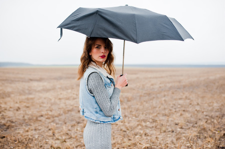 Portrait of brunette curly girl in jeans jacket with black umbrella at field.の写真素材