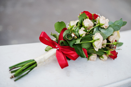 Close-up photo of a bouquet made of beige and red roses and rings on top of it.の写真素材