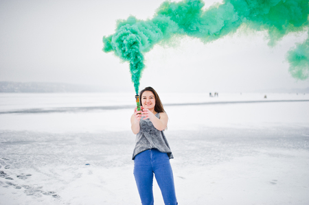 Young girl with green colored smoke bomb in hand in winter day.の写真素材