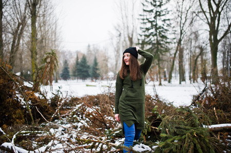 Young girl wear on long green sweatshirt, jeans and black headwear at  branches of the pine tree in winter day.の写真素材