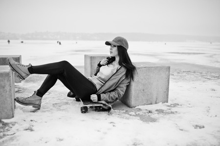 Stylish brunette girl in gray cap, casual street style with skate board on winter day.の写真素材