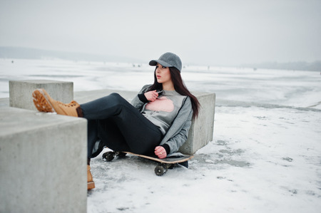 Stylish brunette girl in gray cap, casual street style with skate board on winter day.の写真素材