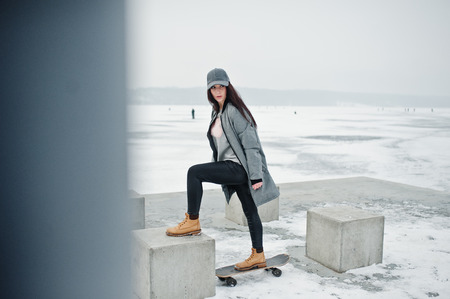 Stylish brunette girl in gray cap, casual street style with skate board on winter day.の写真素材
