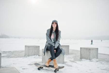 Stylish brunette girl in gray cap, casual street style with skate board on winter day.の写真素材
