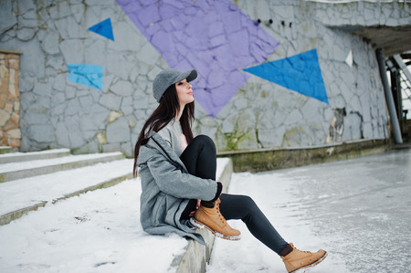 Stylish brunette girl in gray cap, casual street style on winter day against colored wall.の写真素材