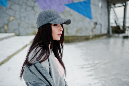 Stylish brunette girl in gray cap, casual street style on winter day against colored wall.の写真素材