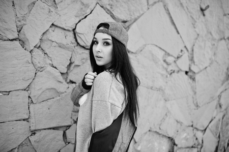 Stylish brunette girl in gray cap, casual street style on winter day against colored wall.の写真素材