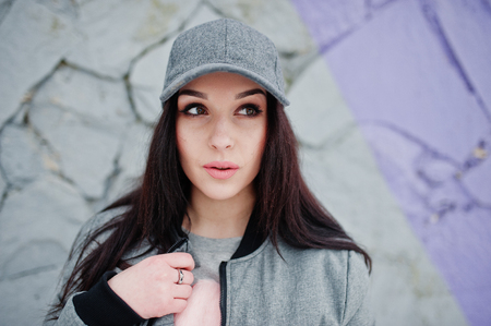 Stylish brunette girl in gray cap, casual street style on winter day against colored wall.の写真素材