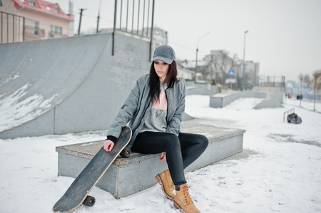 Stylish brunette girl in gray cap, casual street style with skate board on winter day.の写真素材