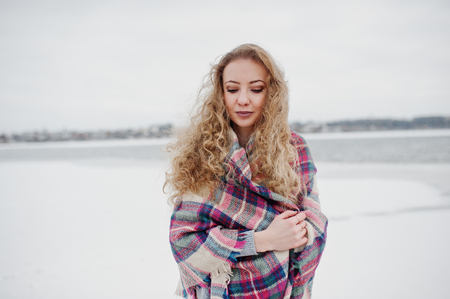 Curly blonde girl in checkered plaid against frozen lake at winter day.の写真素材