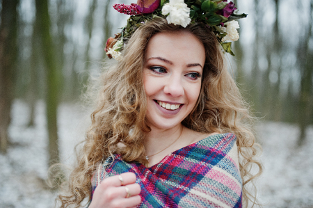Curly cute blonde girl with wreath in checkered plaid at snowy forest in winter day.の写真素材