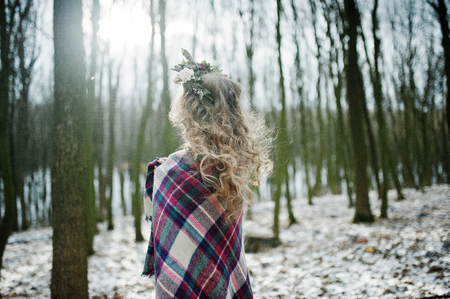 Curly cute blonde girl with wreath in checkered plaid at snowy forest in winter day.の写真素材