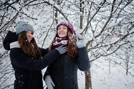 Two funny girls friends having fun at winter snowy day near snow covered trees.