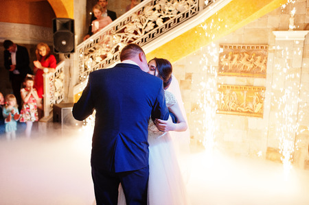 Happy young wedding couple dancing their first dance with different lights and heavy smoke in the restaurant on their wedding party.の写真素材